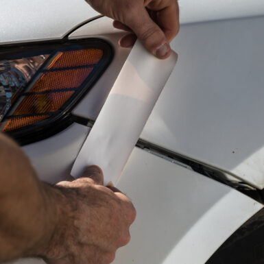 White strip of T-Rex tape being applied to a white car to repair a broken piece